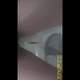 Emi hovers over a hospital toilet next to the grab bars and shits into the bowl, filmed from below. Vertical format video. Over 0.5 minutes.